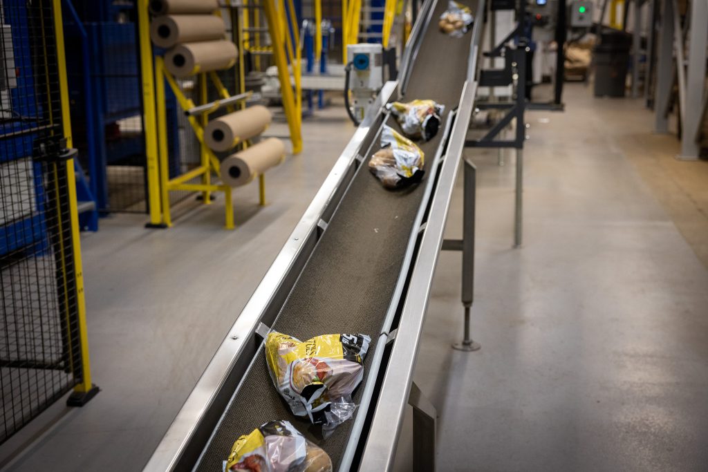 Snack bags on a curved conveyor belt in a factory packaging area.